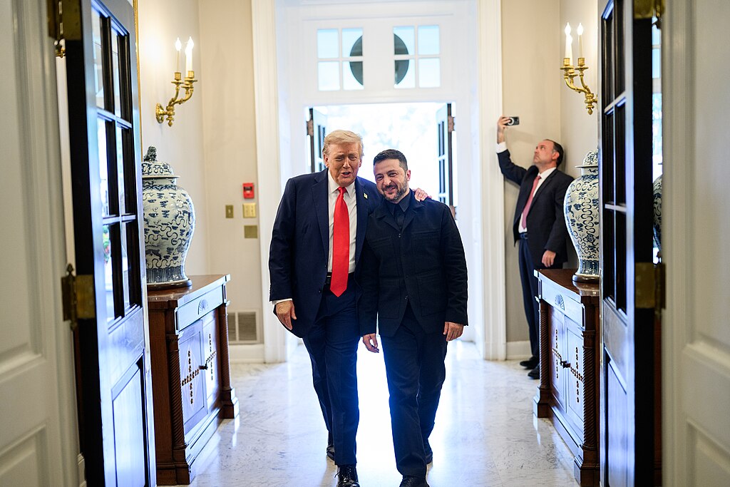Trump and Ukrainian President Zelensky walk side by side through an ornate White House hallway with decorative vases and gold wall sconces during their August diplomatic meeting.