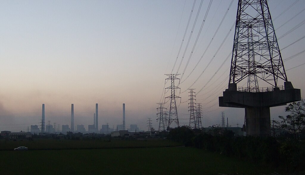The Taichung Power Station in Taiwan with electrical transmission towers and power lines extending across the landscape at dusk.
