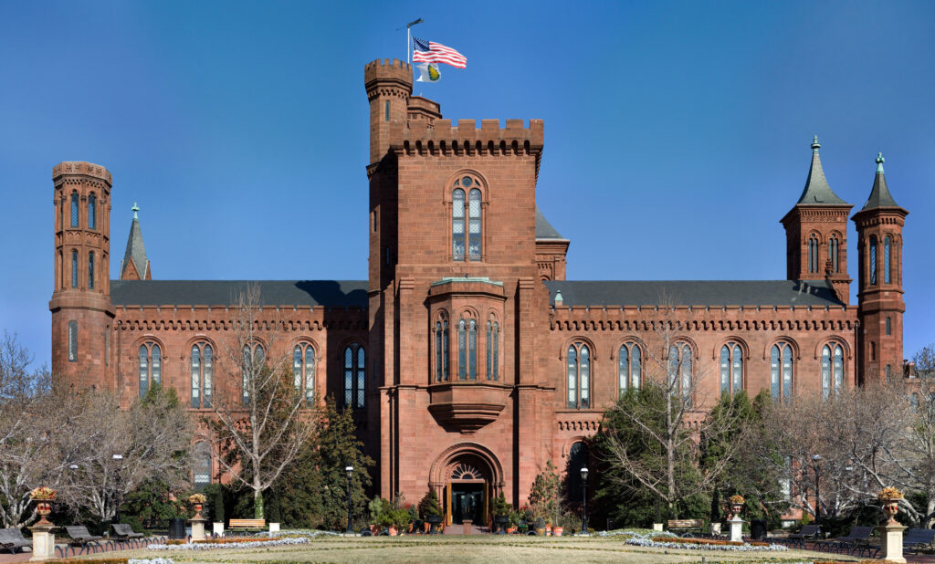 Smithsonian Institution Building in Washington D.C., a red sandstone Gothic Revival structure with towers and American flag.