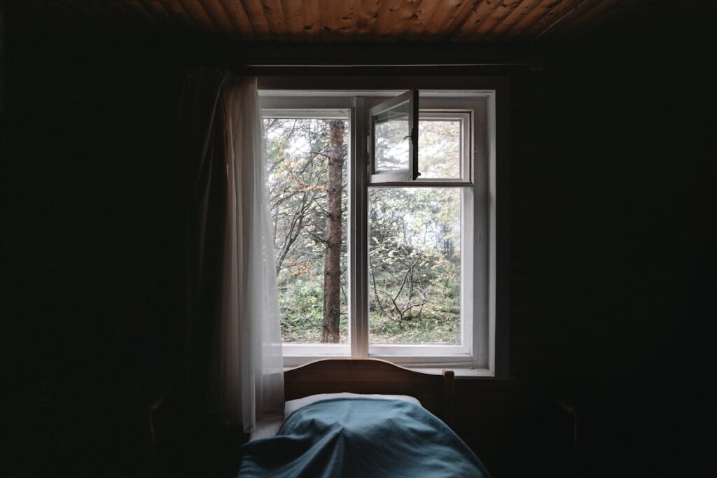 Bed positioned directly under a window with bright sunlight streaming in.