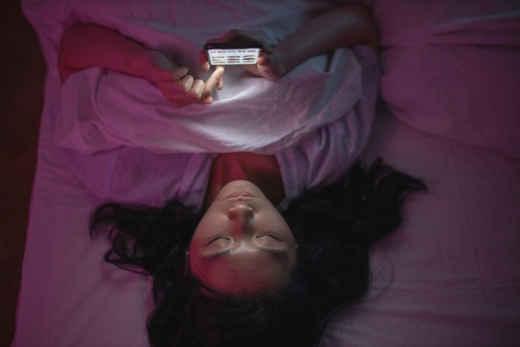 Person using a bright phone screen while lying in bed at night.