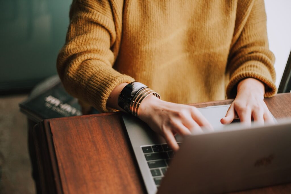 Person in yellow sweater typing on laptop to file AT&T settlement claim.