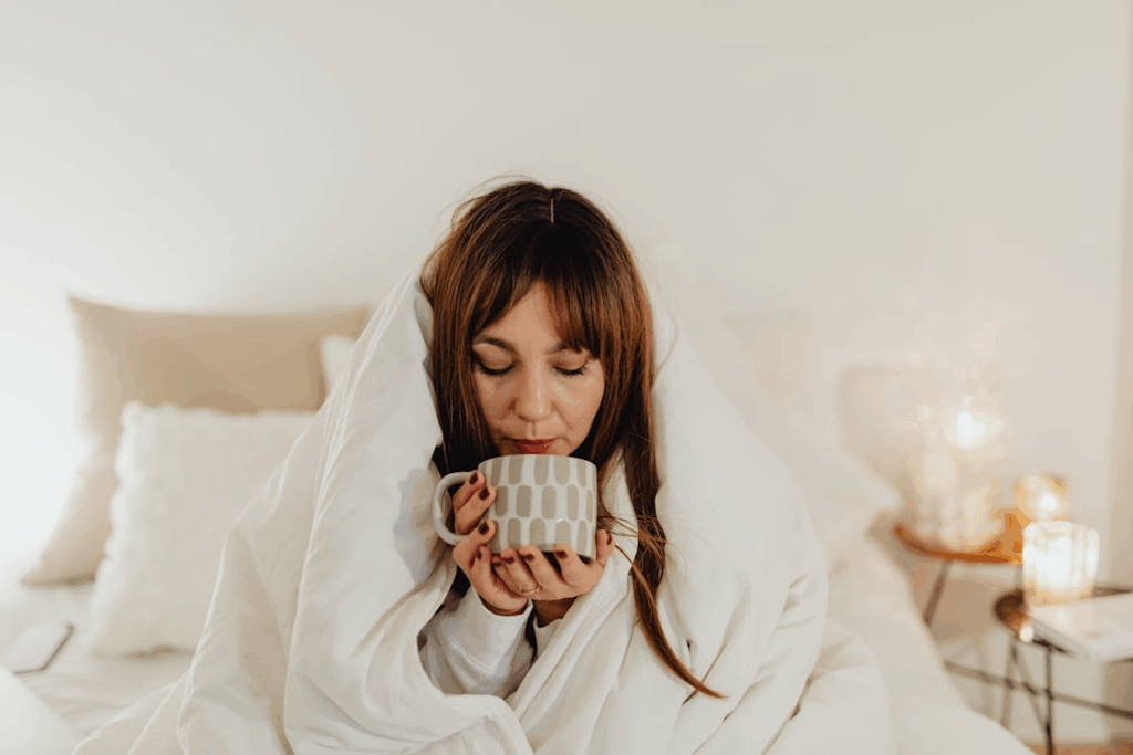 Woman Wrapped in White Blanket Holding a Ceramic Mug