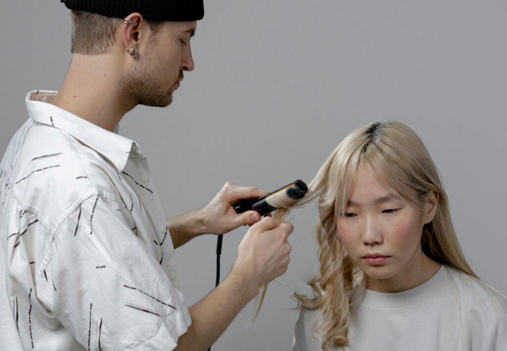 Photo of a Man Using a Curler on a Woman's Hair
