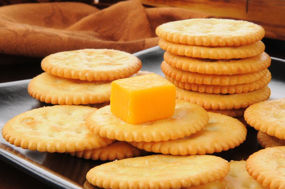 Closeup of a cube of cheddar cheese and wheat crackers
