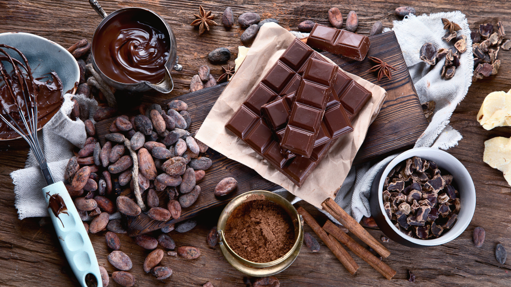 Cacao beans, powder, cacao butter,  chocolate bar and chocolate sauce on wooden background