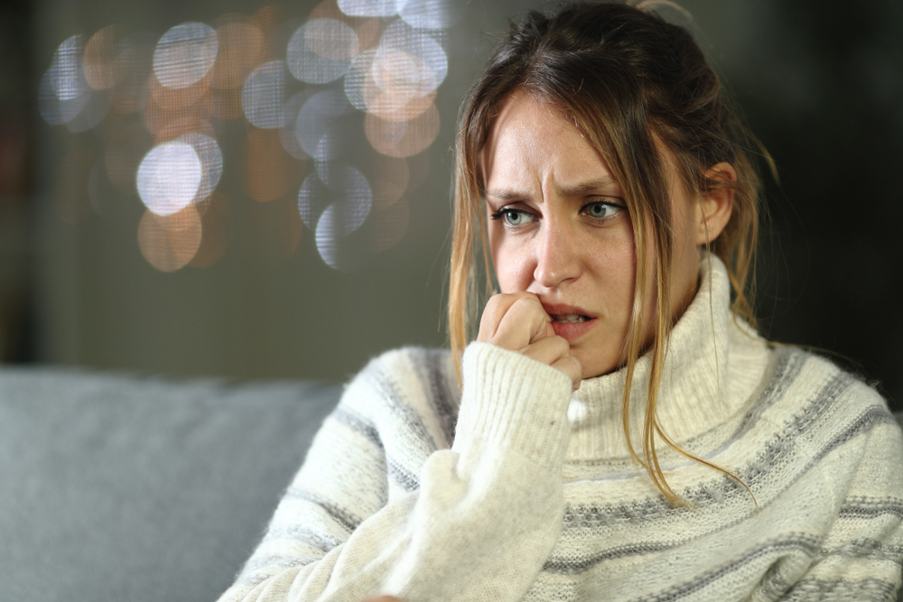 Nervous woman biting nails in winter sitting on a couch in the night at home
