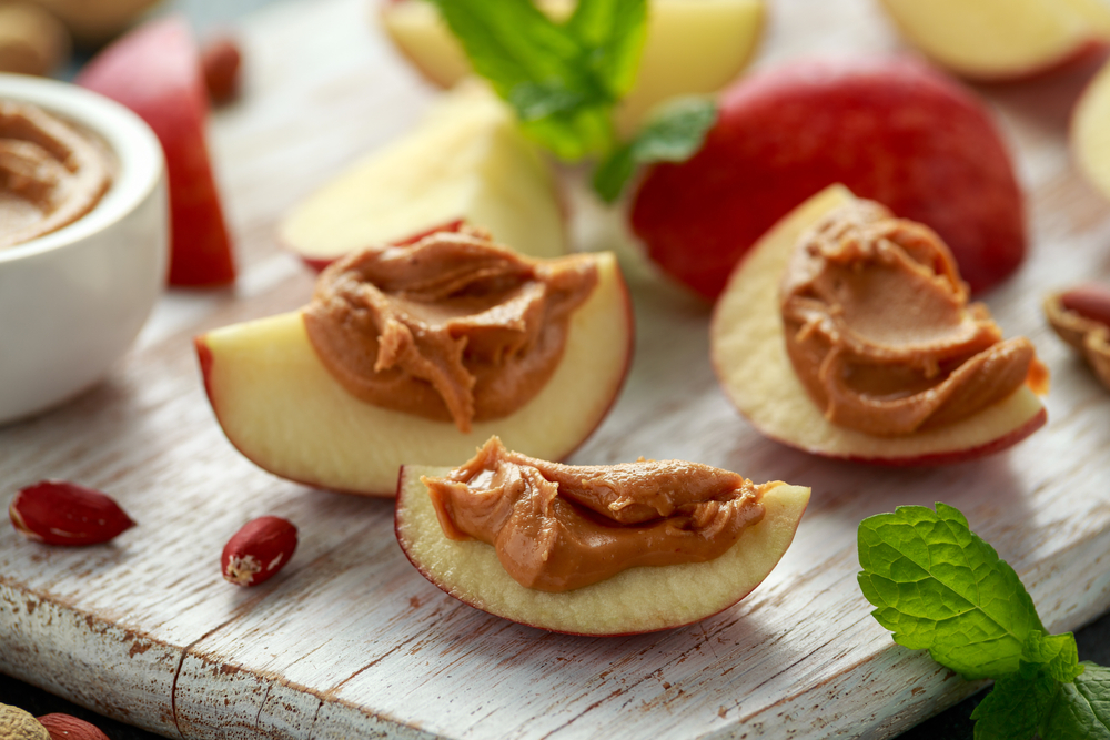 Peanut butter and apple to snack. on white wooden board