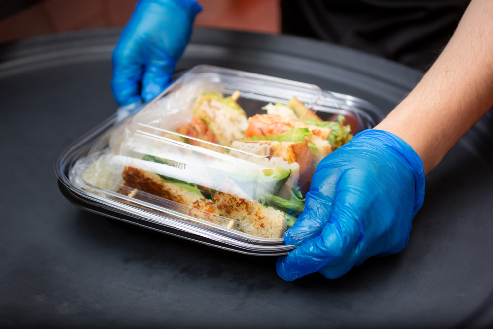 A view of an employee preparing to pack a food to-go containers, in a restaurant kitchen setting.
