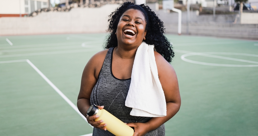 Plus size african woman smiling at camera while doing running routine outdoor - Soft focus on face
