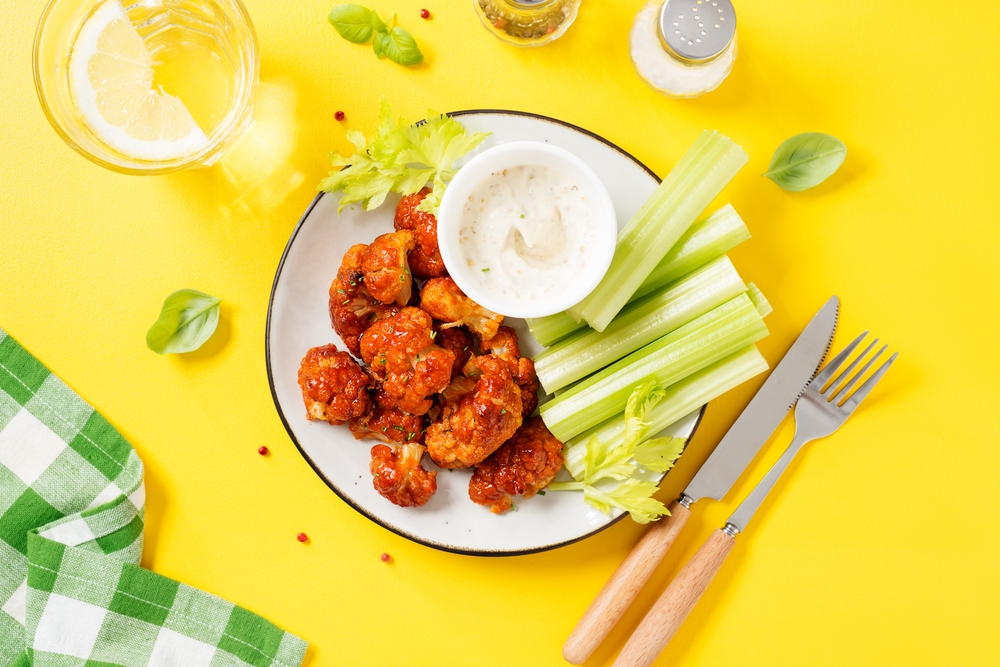 Buffalo style barbecue cauliflower with fresh celery sticks and sauce . Yellow background. Top view.	