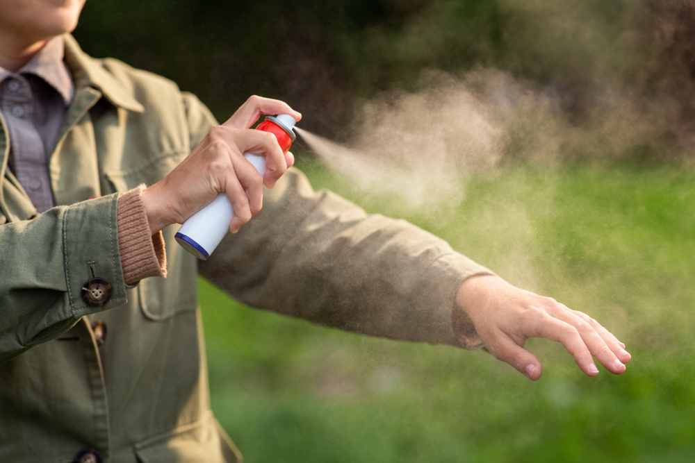 health care, protection and people concept - woman spraying insect repellent or bug spray to her hand at park