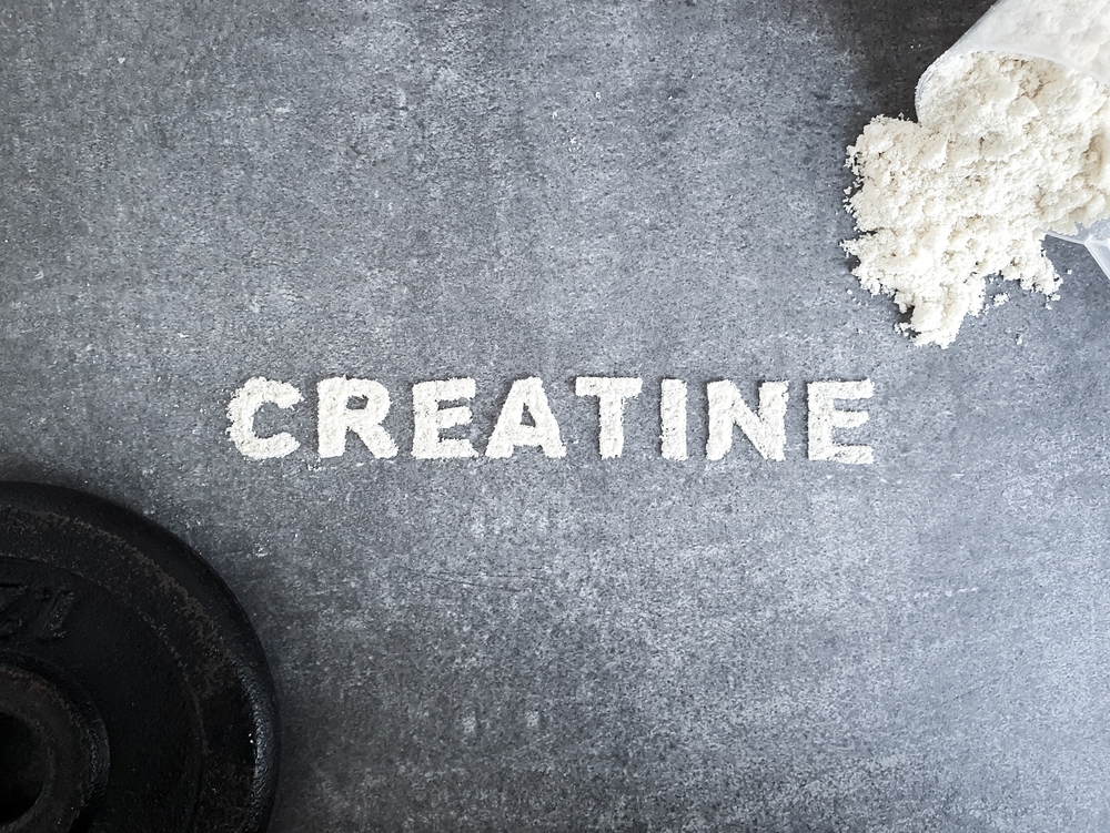 Creatine powder text font for Creatin popular sports supplement used to icrese muscle mass on stone background with scoop of creatine powder and sumbbell concept