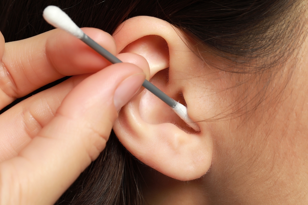 Woman cleaning ear with cotton swab, closeup
