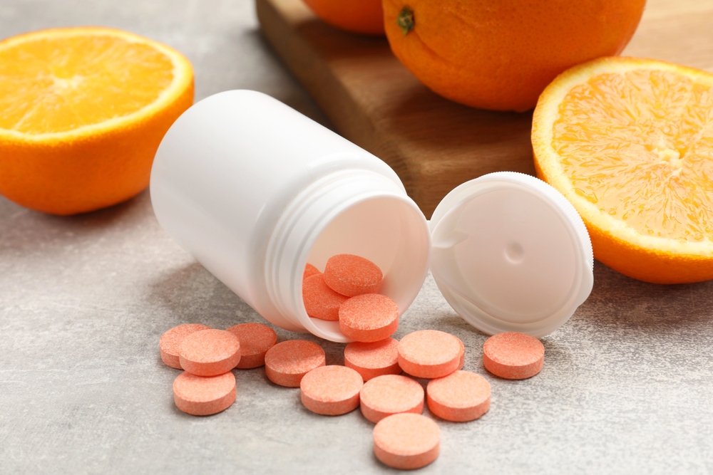 Dietary supplements. Overturned bottle, pills and oranges on grey table