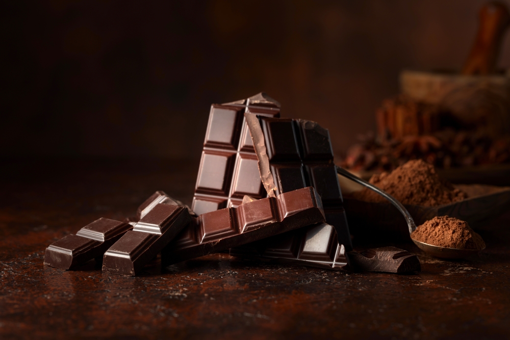 Broken dark chocolate bar and cocoa powder on a brown table. Copy space.