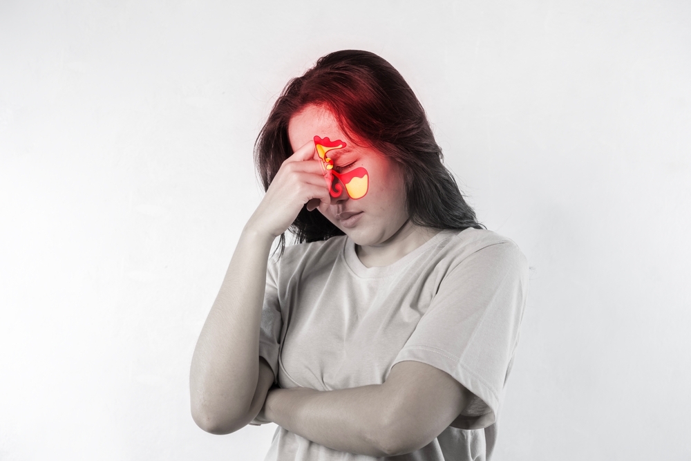 A woman with a red nose and red eyes. She has her hands on her head. Sinusitis, frontitis. Female face with inflammation of mucous membrane of paranasal and frontal sinuses.