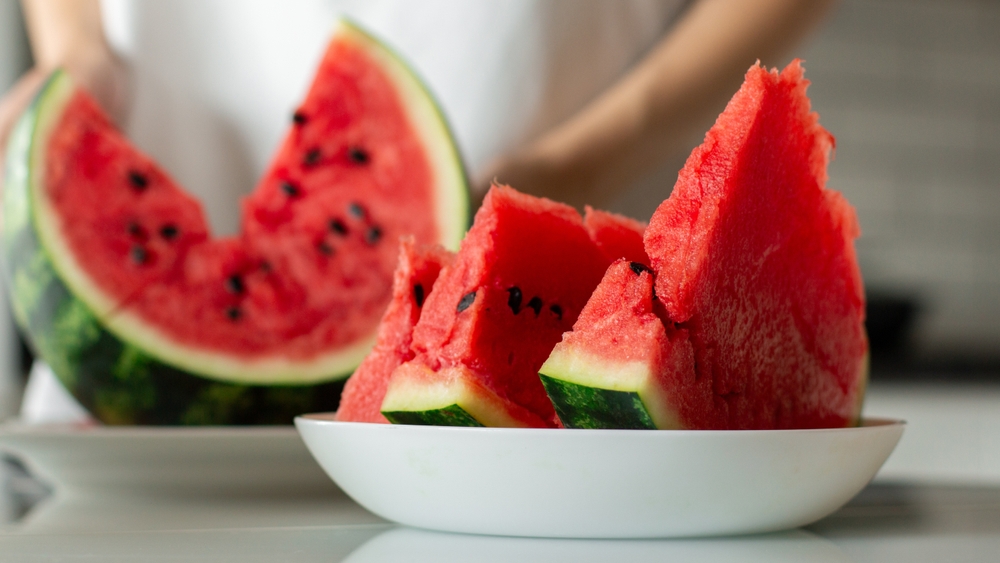 Woman with slice of fresh watermelon at kitchen, closeup
