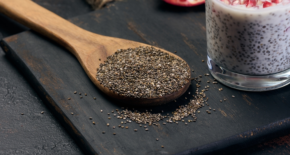 Chia seeds in a wooden spoon on a black table, close up