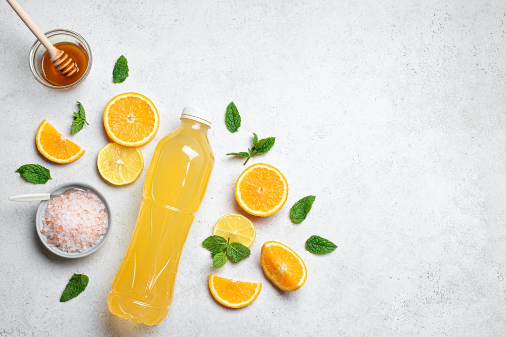 Orange Isotonic energy drink. Bottle of homemade sport electrolyte water with hymalayan salt, citrus fruits and honey on white background, top view, copy space. Fitness drink template.
