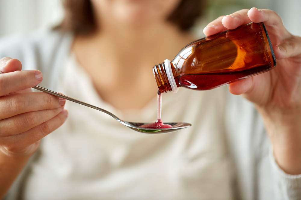 healthcare, people and medicine concept - woman pouring medication or antipyretic syrup from bottle to spoon
