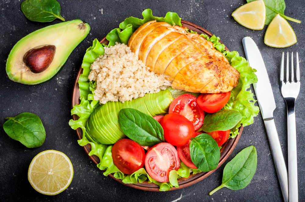 Healthy dinner with quinoa, chicken, tomatoes, avocado, spinach and lettuce leaves. Buddha bowl. Healthy salad bowl on dark background. Top view
