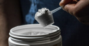 scoop of creatine being taken from large white tub containing the white crystalline powder