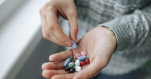 person taking a pill from pile of pills in one other their hands
