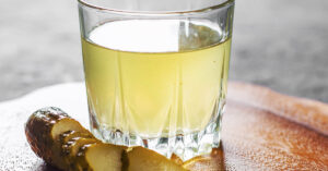 Glass of pickle juice or brine on table with a sliced pickle beside it
