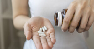 woman dispensing white pills into palm of hand.