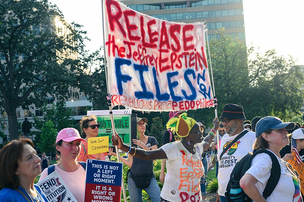 Protesters holding signs demanding "RELEASE The Jeffrey EPSTEIN FILES" and "THIS IS NOT A LEFT OR RIGHT MOMENT. IT IS RIGHT OR WRONG MOMENT" during a rally.