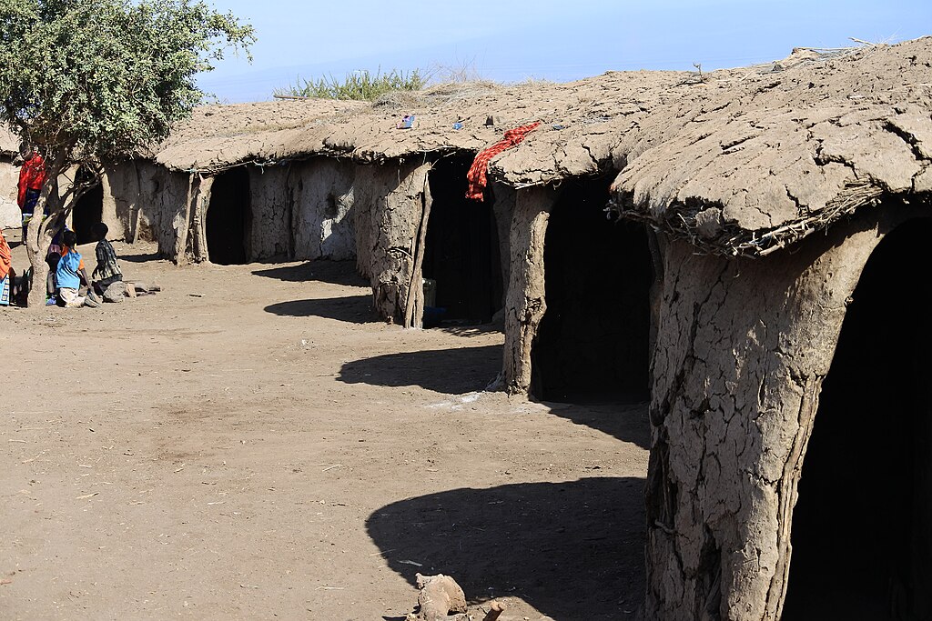 Maasai mud huts with thatched roofs surrounding a dusty village courtyard in rural Kenya.