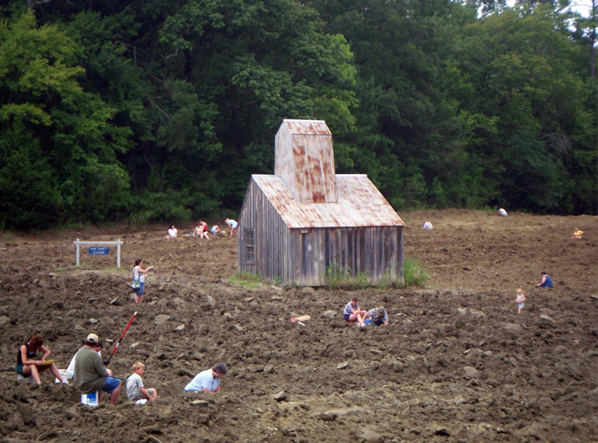 Visitors with tools searching through plowed dirt field at the diamond mine, wooden shed is also visible.