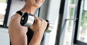 At 70, She Lost 68 Pounds, Reversed Arthritis, Quit Meds and Gained 1.9M Followers by Following These 5 Daily Habits positive sportswoman in wireless earphone exercising with dumbbell in gym