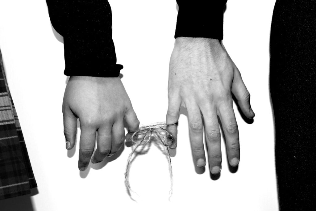 Two hands with pinky fingers bound together with rope in black and white.
