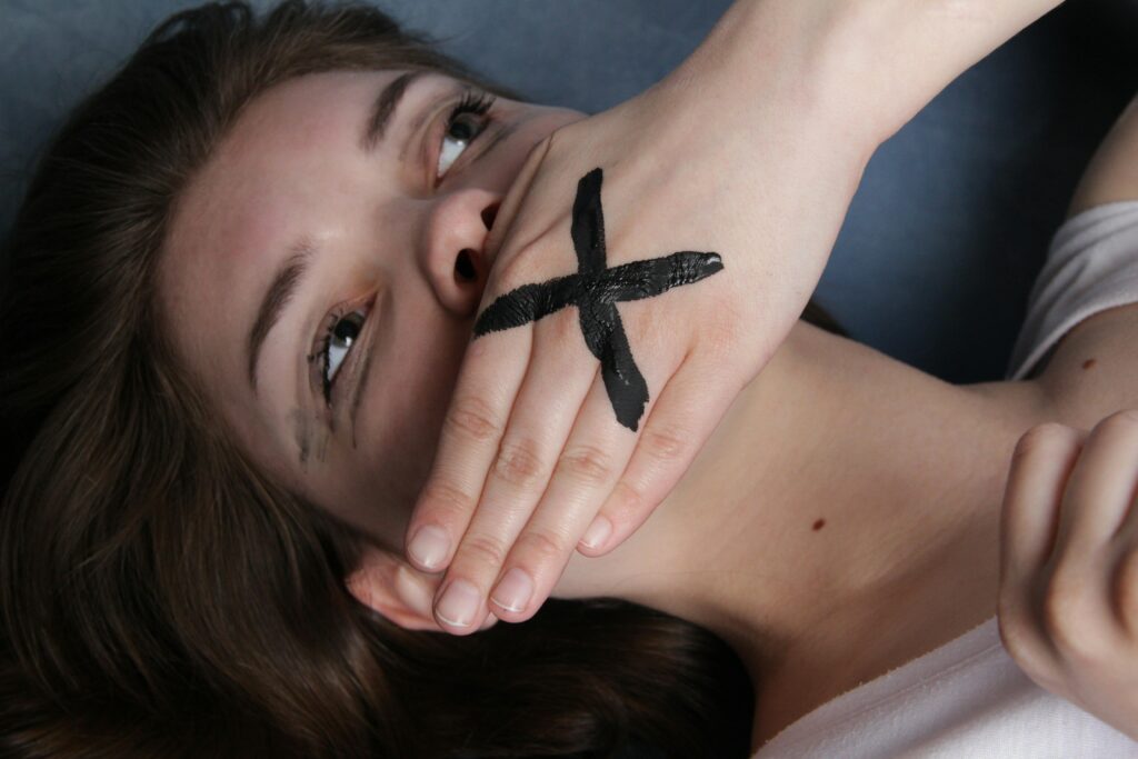 Woman covers mouth with hand, black cross drawn over the top of her hand, representing silencing from things narcissists say.