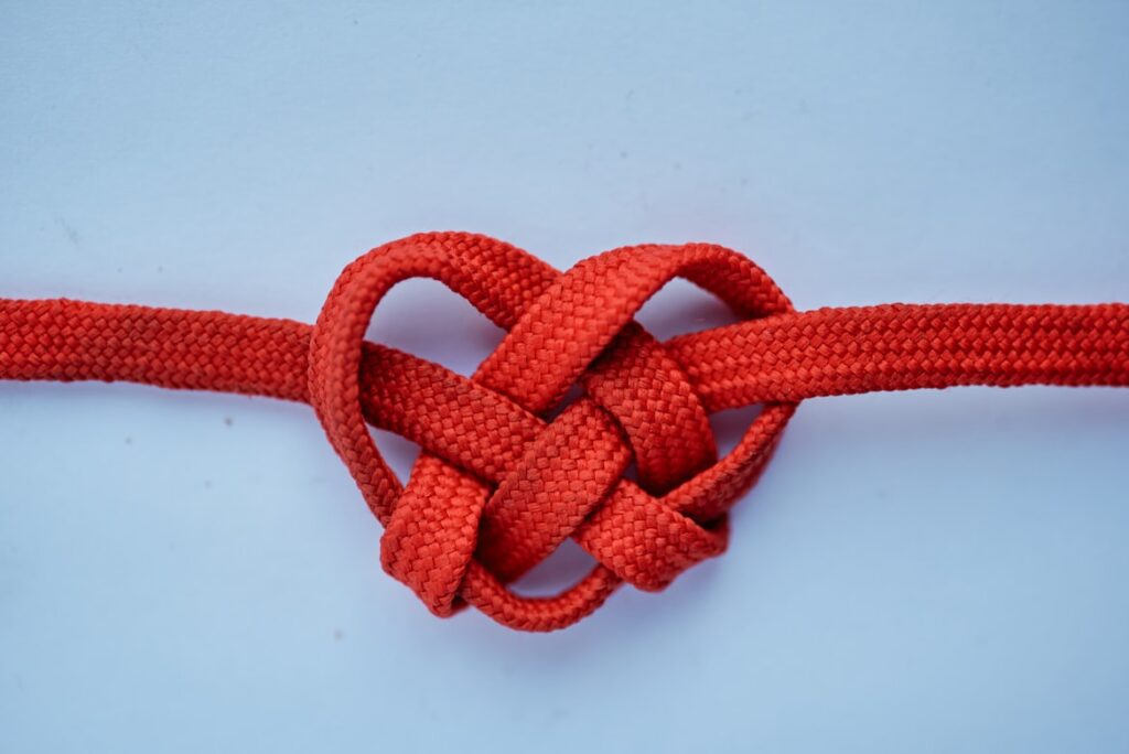 Red rope tied into heart-shaped knot against white background.