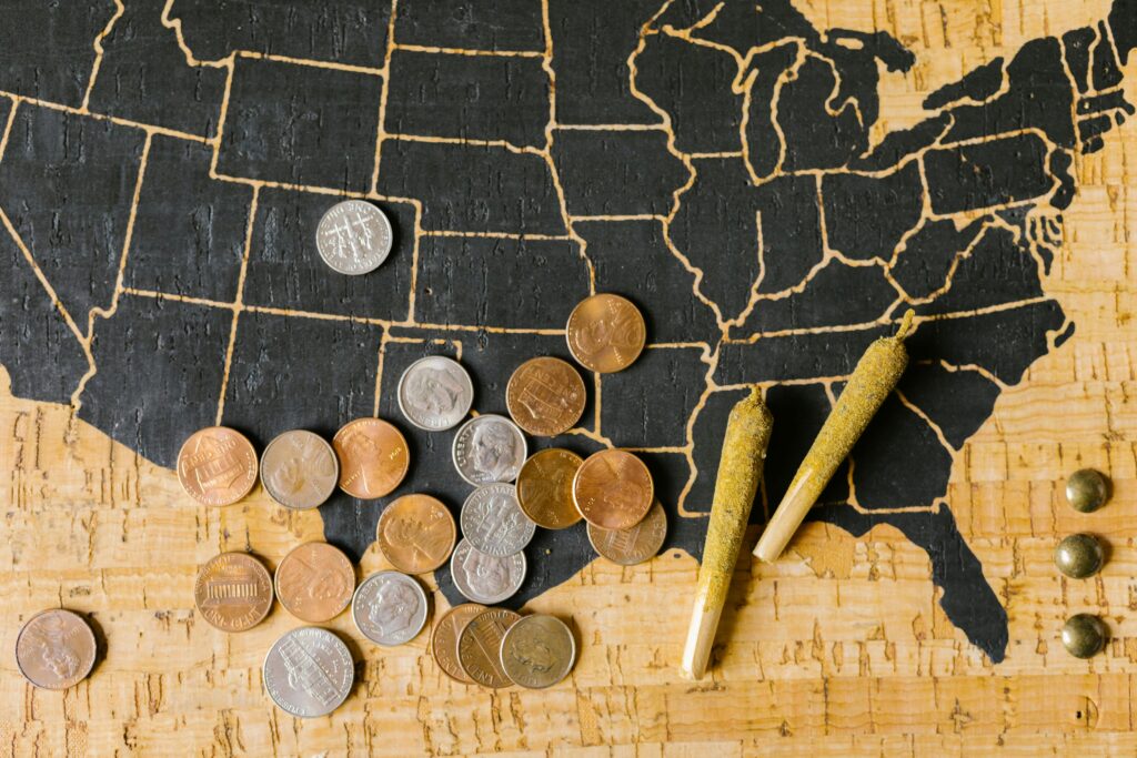 US map with scattered coins and cannabis joints representing state tax revenue opportunities from marijuana policy changes.