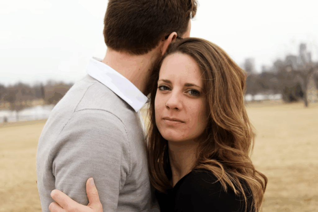 Couple embraces outdoors, woman appears distant while man holds her close.