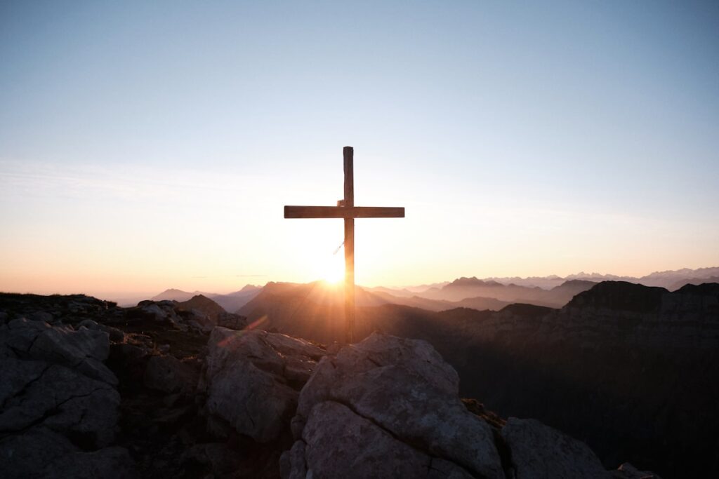 Wooden cross silhouetted against golden sunrise over mountain landscape, symbolizing Christian hope and faith in Christ's return.