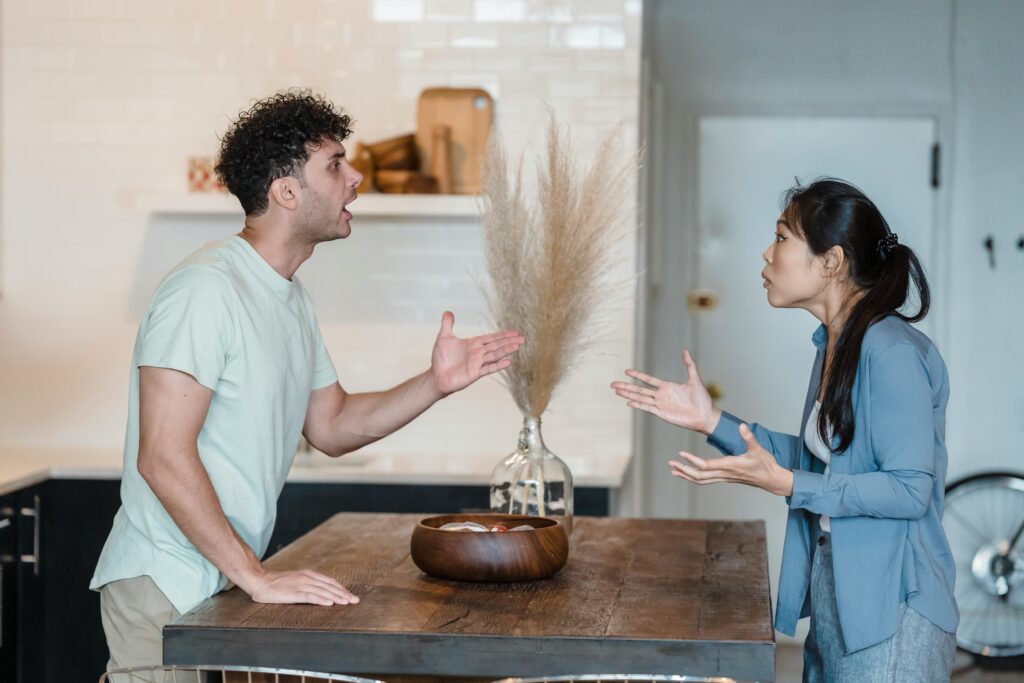 Couple standing in kitchen having tense discussion with hands gesturing.