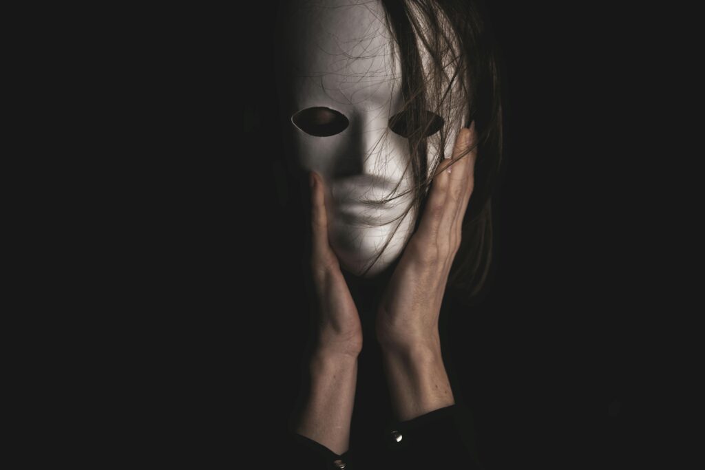 Hands hold white theatrical mask against dark background.