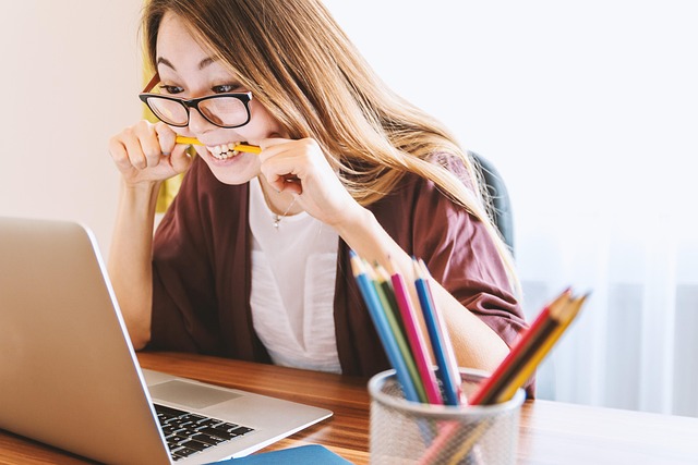 woman biting pencil while working on laptop