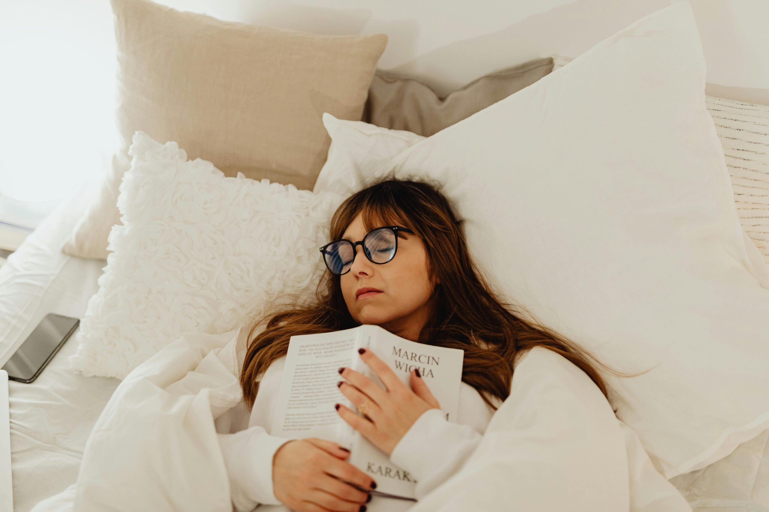 A woman is holding a book lying down with eyeglasses