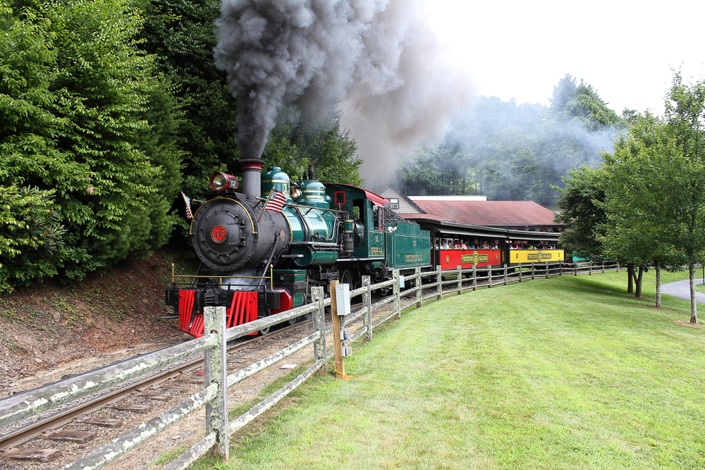 Boone, North Carolina / USA - 07/14/2018: The big toy train at Tweetsie Railroad theme park for kids up in the smokey mountains with black smoke and tourist passengers having a good run time.