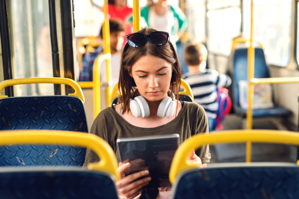 Pretty young girl with headphones sitting in a bus and watching tablet.