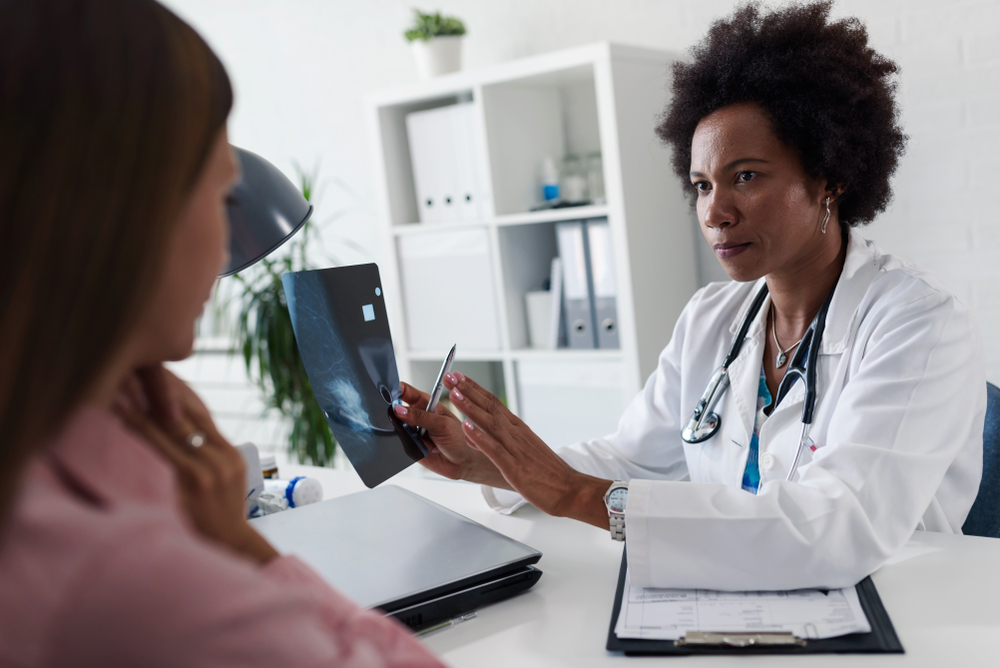 A female doctor sits at her desk and talks to a female patient while looking at her mamogram. Brest cancer prevention