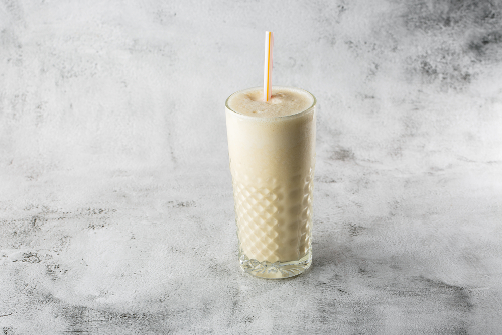 Banana oats smoothie or vanilla milkshake in glass on bright marble background. Overhead view, copy space. Advertising for milkshake cafe menu. Horizontal photo.