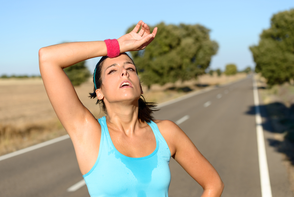Tired runner sweating after running hard in countryside road. Exhausted sweaty woman after marathon training on hot summer. Hispanic brunette female athlete outdoors.