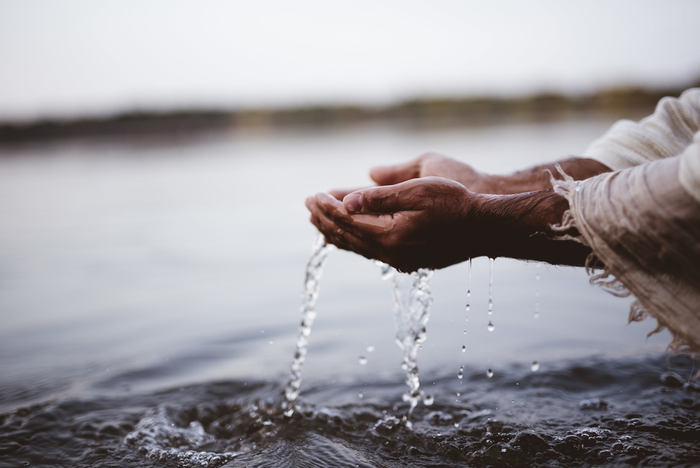 A closeup shot of a person wearing a biblical robe drinking water with hands

